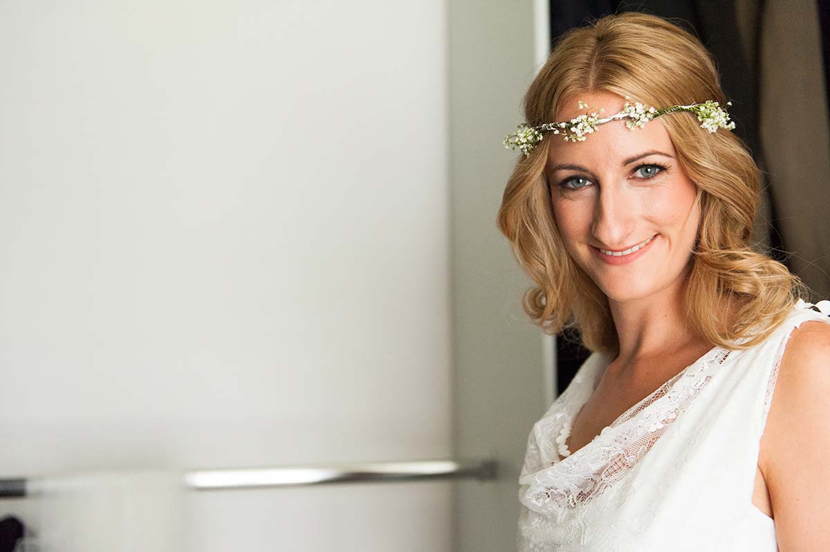 Honeylight Hochzeitsfotografen: Braut im Brautkleid in Hochzeitsvorbereitung blickt glücklich in die Kamera