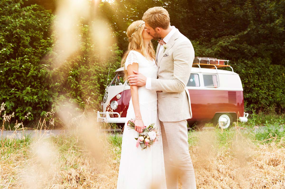 Honeylight Hochzeitsfotografen: Brautpaar küsst auf einem Feld. Im Hintergrund ein roter VW Bulli